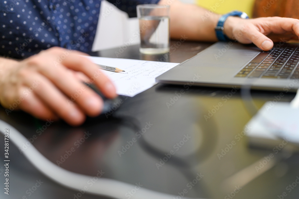 work from home. workplace with a laptop, glass of water and paper for notes. working man. male hands using a computer mouse and keyboard. selective focus work from home. workplace with a laptop, glass of water and paper for notes. working man. male hands using a computer mouse and keyboard. selective focus