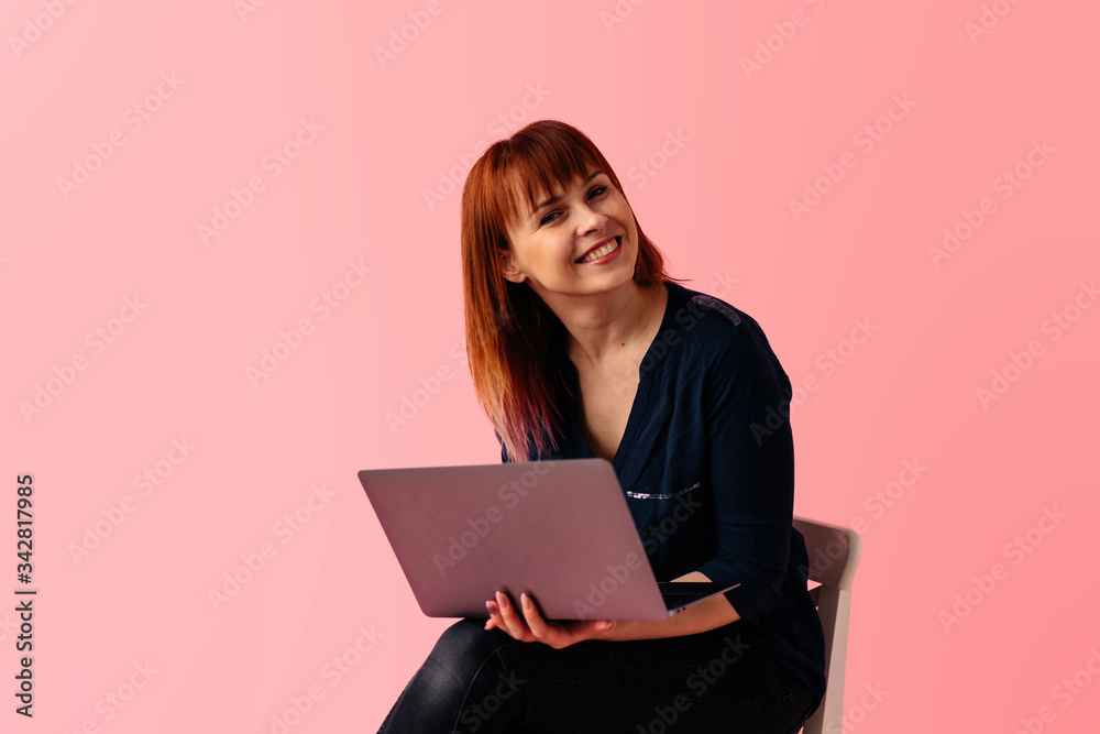 Young businesswoman working on the laptop sitting on tha chair in studio isolated on pink background Young businesswoman working on the laptop sitting on tha chair in studio isolated on pink background