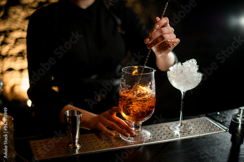 Close-up. Woman bartender mix cold cocktail with spoon in glassy mixing cup.