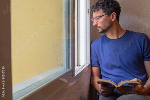 Bild auf Leinwand chico deprimido confinado en casa en la ventana leyendo