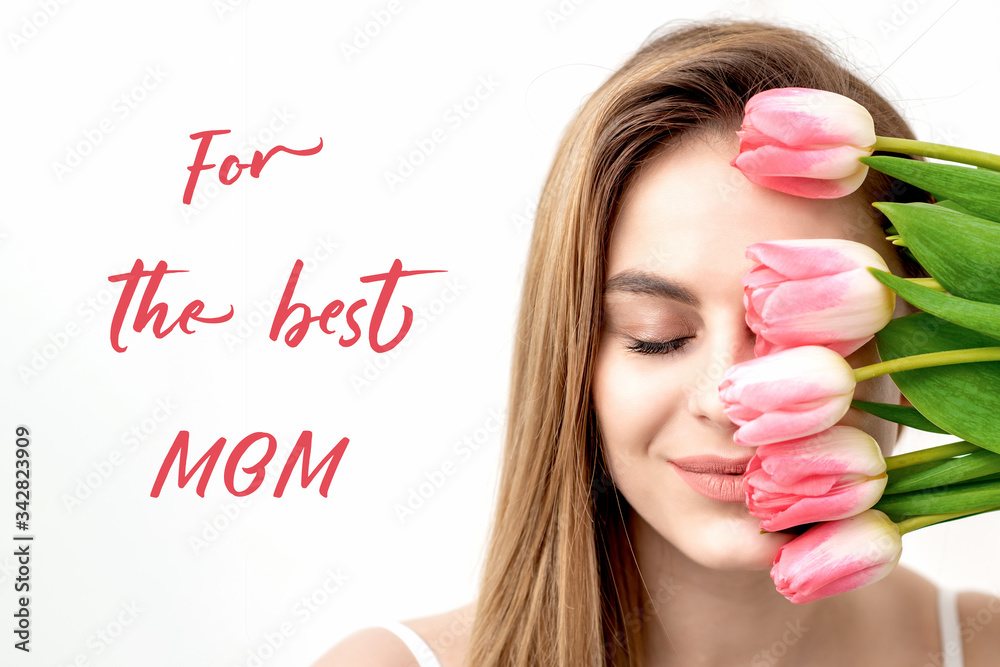 Smiling young woman with pink tulips, sign text For The Best Mom on white background. Mother's day celebration card.