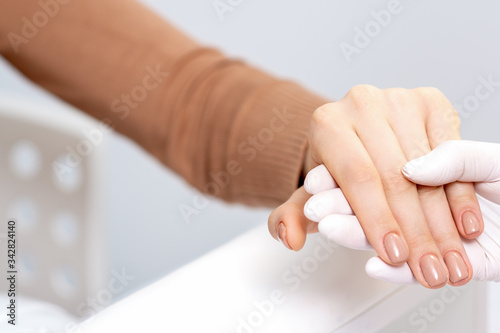 Manicurist hand is holding woman hand with beige manicure close up.