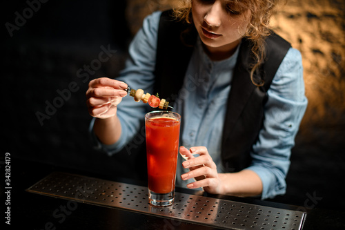 Lady at bar gently decorates glass with Bloody Mary cocktail