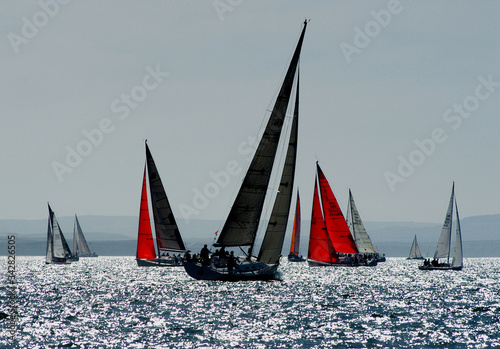 Fotografie, Obraz Red sails and yachts sailing in the round the island race off The Isle of Wight