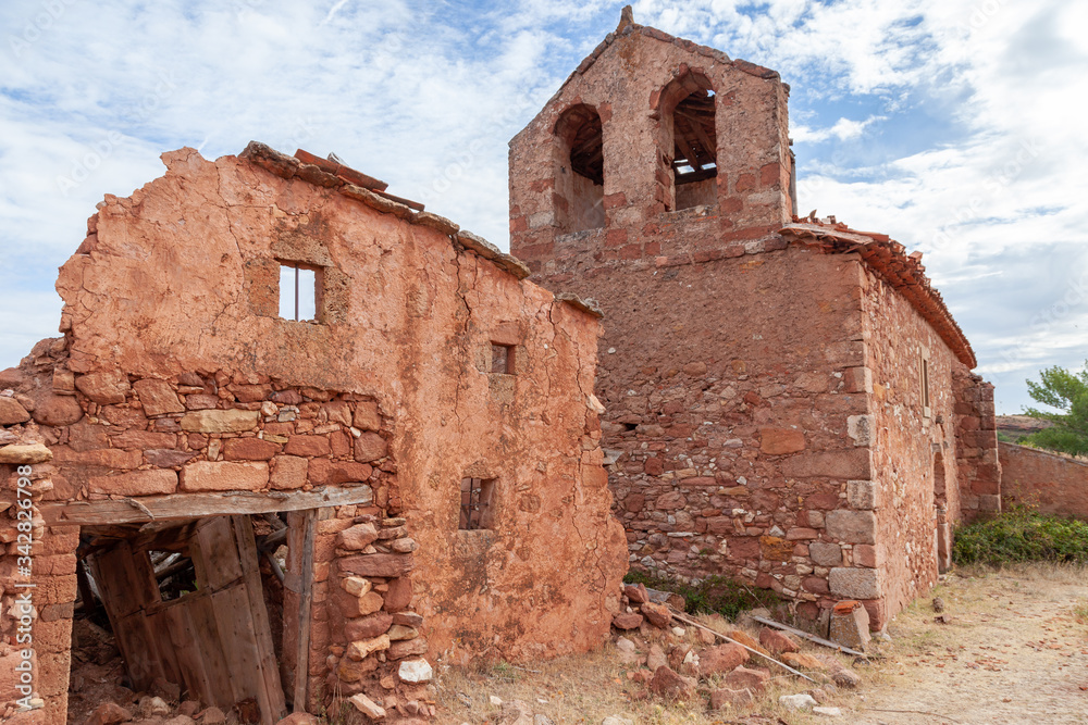 Ruins of a house of red stone, near a church in an abandoned village 