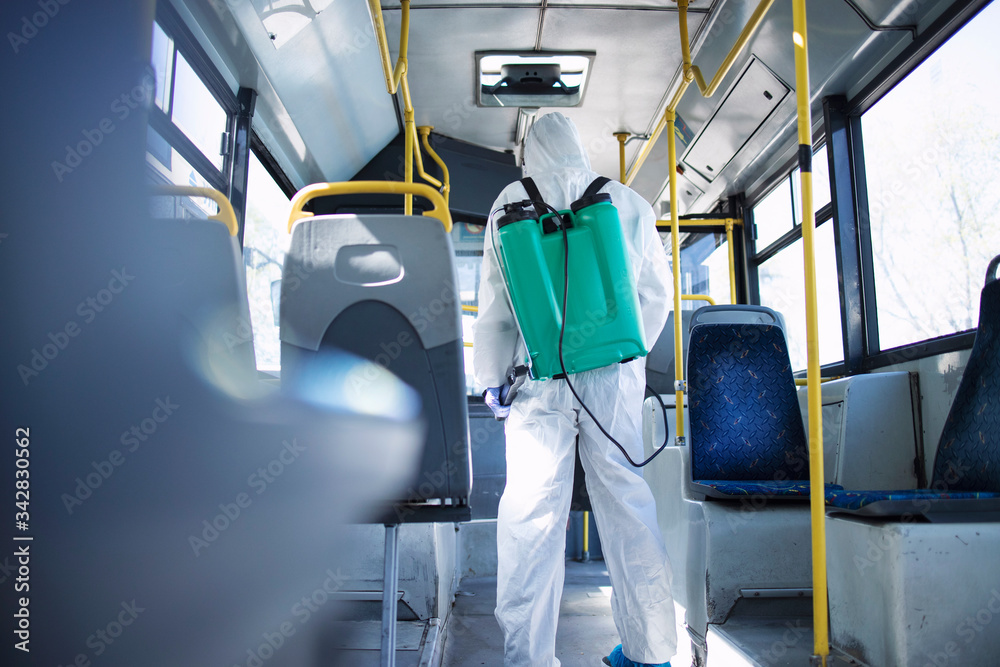 Public transportation healthcare. Man in white protection suit disinfecting and sanitizing handlebars and bus interior to stop spreading highly contagious coronavirus or COVID-19. Public transportation healthcare. Man in white protection suit disinfecting and sanitizing handlebars and bus interior to stop spreading highly contagious coronavirus or COVID-19.