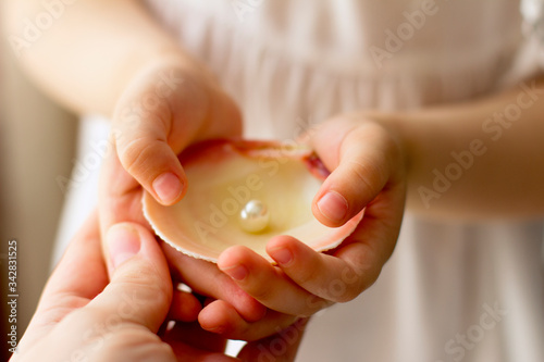 
Mom and baby hands hold oyster shell with pearls