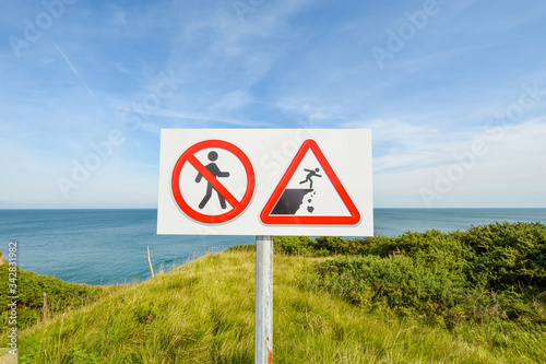 A sign warning visitors to be cautious walking and avoid crumbling rocks on the cliff at the WWII battle site of Pointe du Hoc, in Normandy, France