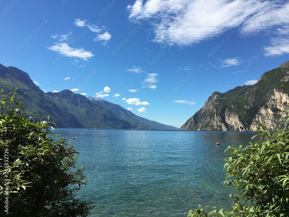 View from the lakeside of Riva del Garda in Italy looking out over the crystal clear waters of the lake, with tall mountains in the background