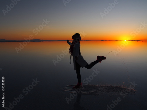 Girl model with long black hair in the white coat  red scarf and red headphones on the sunrise  Uyuni Salt Flat  Salar de Uyuni  Bolivia. Copy space for text