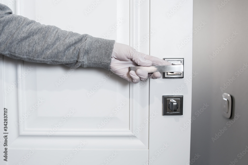 Female hand in medical protective gloves to protect hands from infection or virus touches the door handle. Coronavirus pandemic infection. COVID-19. WHO recommendations Female hand in medical protective gloves to protect hands from infection or virus touches the door handle. Coronavirus pandemic infection. COVID-19. WHO recommendations
