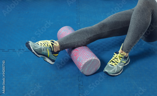 Fit woman using a foam roll on her leg to release tension and help with muscle pain after training in gym photo