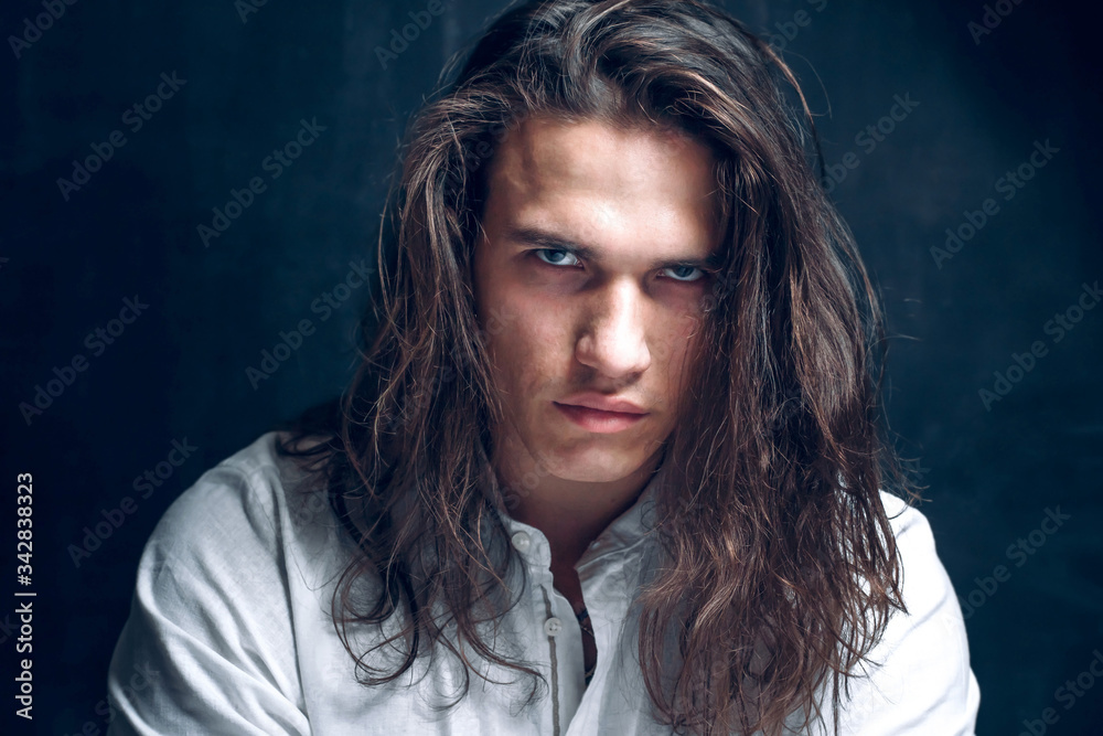 Handsome calm man. Portrait of a young muscular guy with long hair. Strong boy on an isolated dark background in the studio - obrazy, fototapety, plakaty 
