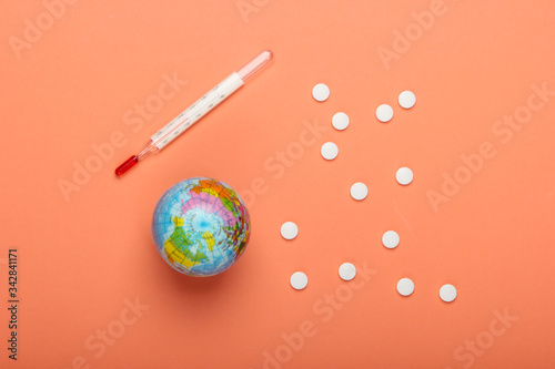 Global pandemic still life. Globe  thermometer with pills on orange background. Coronovirus outbreak