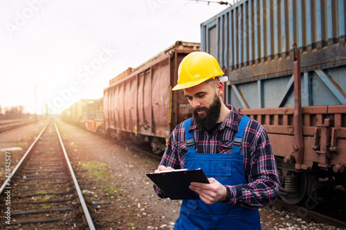 Dispatching cargo containers via railroad freight transportation. Shipping worker writing down on clipboard and controlling shipping cargo containers departure. Organizing goods export. photo