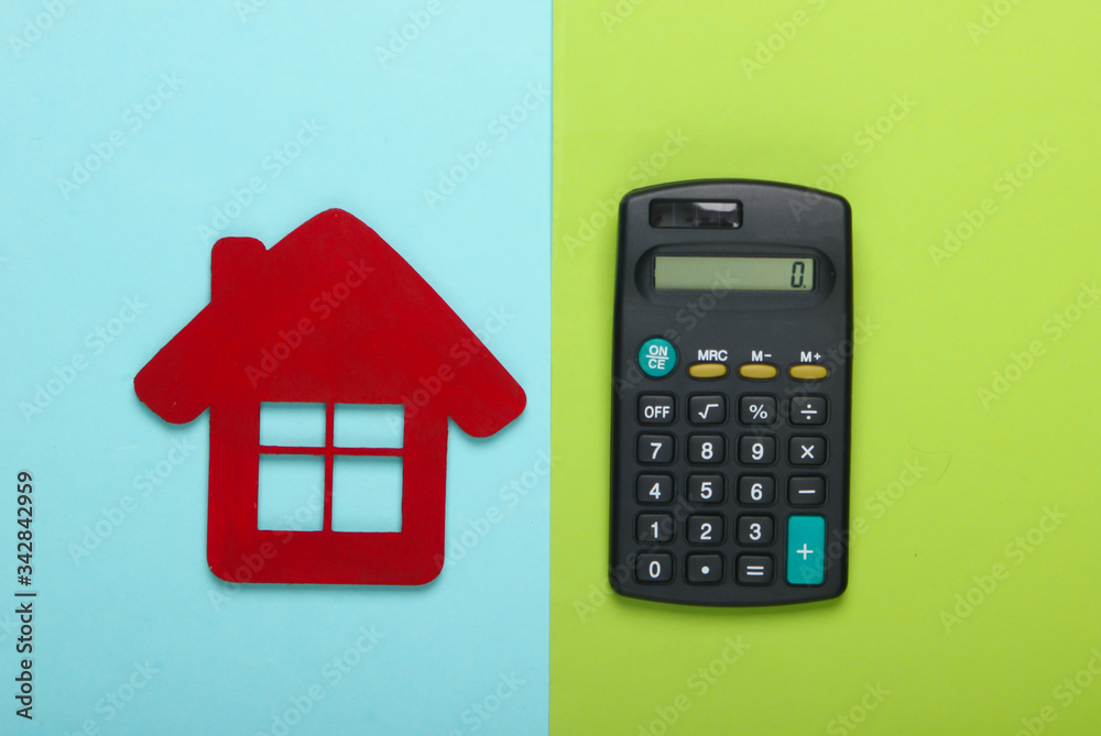 Calculation of the cost of rental housing. Red house figurine, calculator on a blue-green background. Top view Calculation of the cost of rental housing. Red house figurine, calculator on a blue-green background. Top view