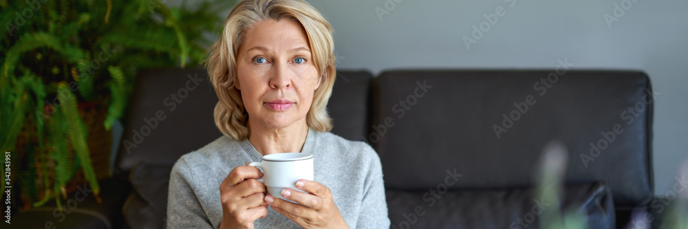 Delicious drink.Elderly woman sitting on the sofa in her living room and holding a cup of coffee Delicious drink.Elderly woman sitting on the sofa in her living room and holding a cup of coffee