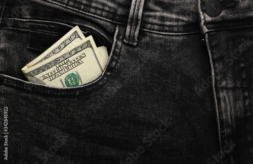 Hundred dollar bills in the front pocket of black jeans close-up.