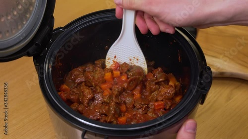 a man cooks the beef in a slow cooker, mixing it with a spoon