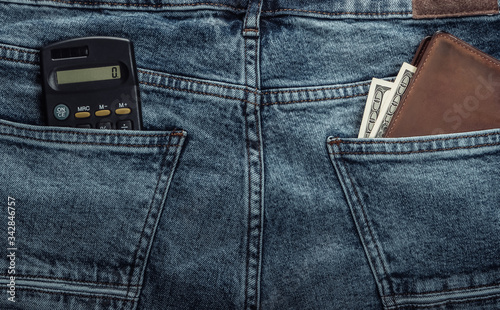 Calculator and wallet with dollars in the back pockets of blue jeans