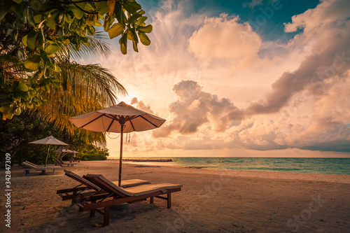 Beautiful tropical sunset scenery  two sun beds  loungers  umbrella under palm tree. White sand  sea view with horizon  colorful twilight sky  calmness and relaxation. Inspirational beach resort hotel