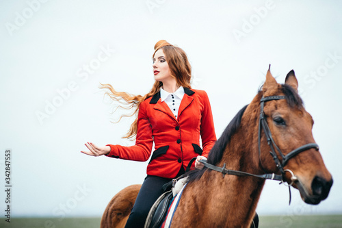 red-haired jockey girl in a red cardigan and black high boots with a horse