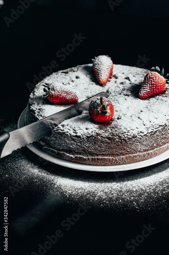 Chocolate cake with strawberry on wooden table black background cutting one slice with knife dark food photo