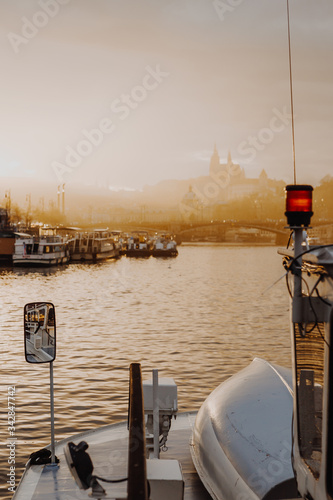 view from the upper deck of a tourist boat sailing along the Vltava River under Charles Bridge overlooking a hill with an ancient church at sunset