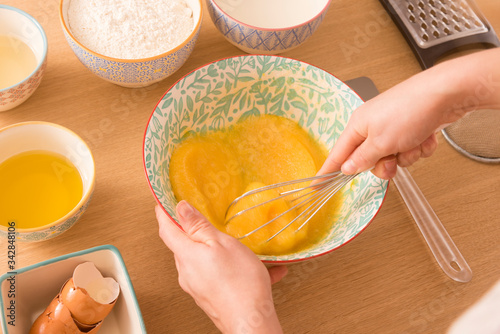 Fotomural chica batiendo huevos y azúcar para hacer magdalenas en casa, ingredientes en bo