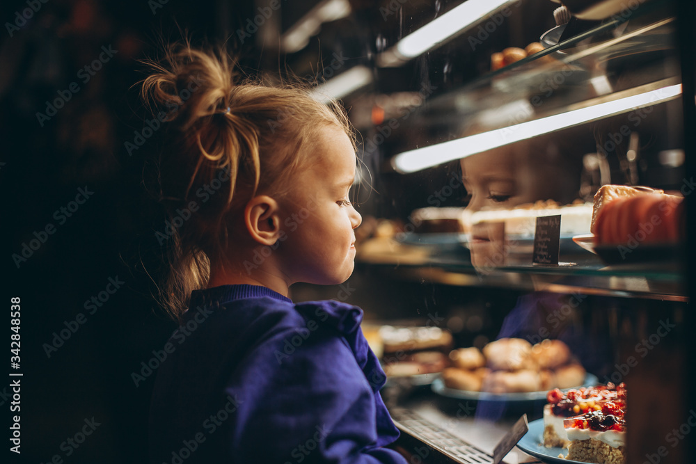 lovely girl admiringly examines a lighted showcase with various delicious cakes and desserts