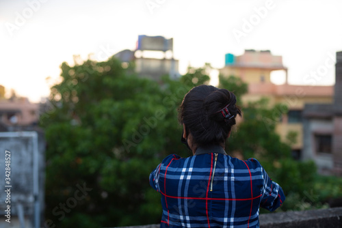 Back side portrait of an Indian young woman with corona preventive mask on a rooftop  in home isolation.Indian lifestyle, disease and home quarantine.