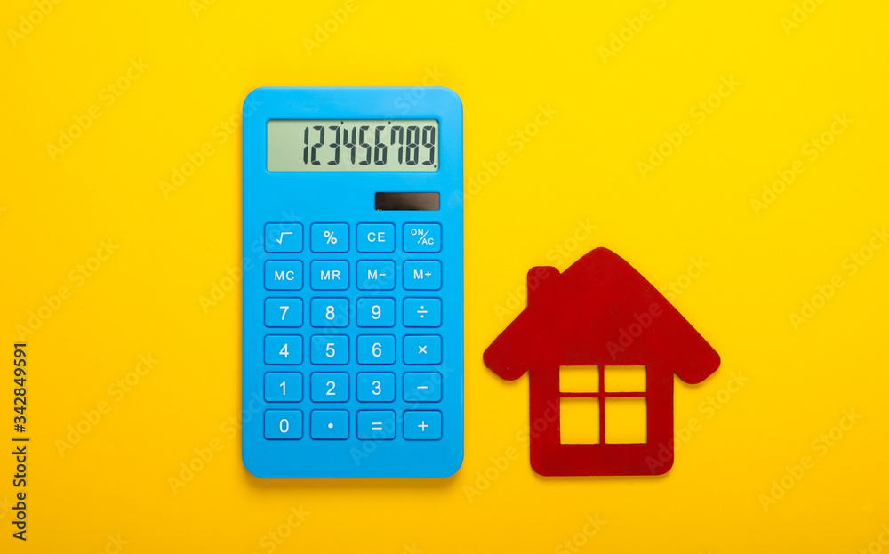 Calculation of the cost of rental housing. Red house figurine, calculator on yellow background. Top view Calculation of the cost of rental housing. Red house figurine, calculator on yellow background. Top view