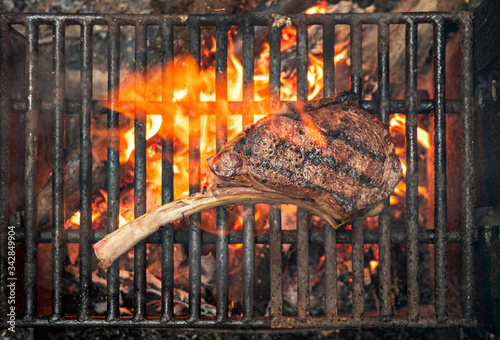 tomahawk steak cooking on flaming grill photo