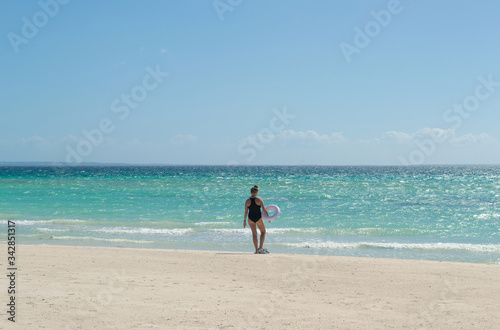 Young woman in closed swimsuit with swimming circle undressing on sand deserted beach by the sea in Philippines