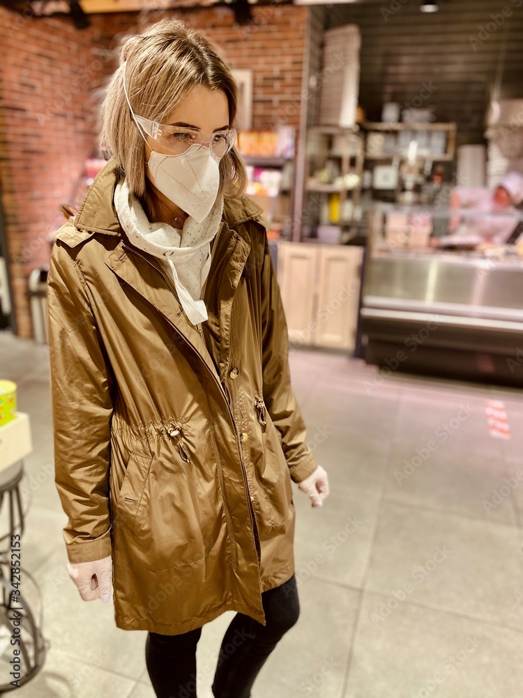 young woman shopping in supermarket. beautiful girl in a protective flu mask, goggles and gloves in a store, holds goods, purchases during quarantine - against coronavirus