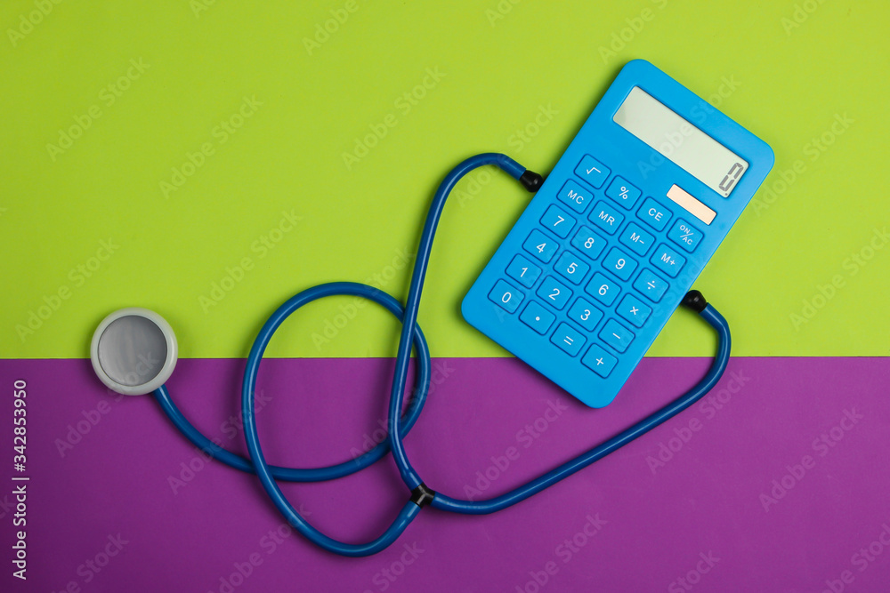 Health Care Concept. Calculator with a stethoscope on a green purple background. Top view