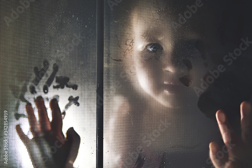 Little girl behind blur window. Baby look at you through the glass