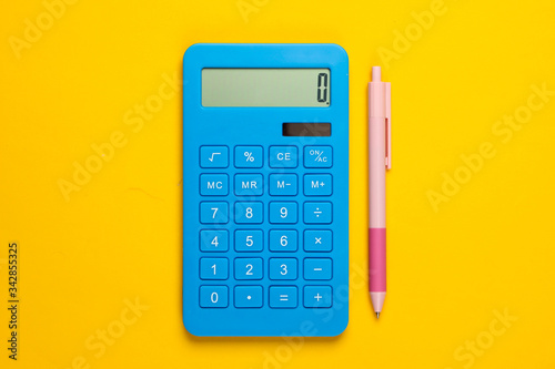 Blue calculator with pen on yellow background. Top view.