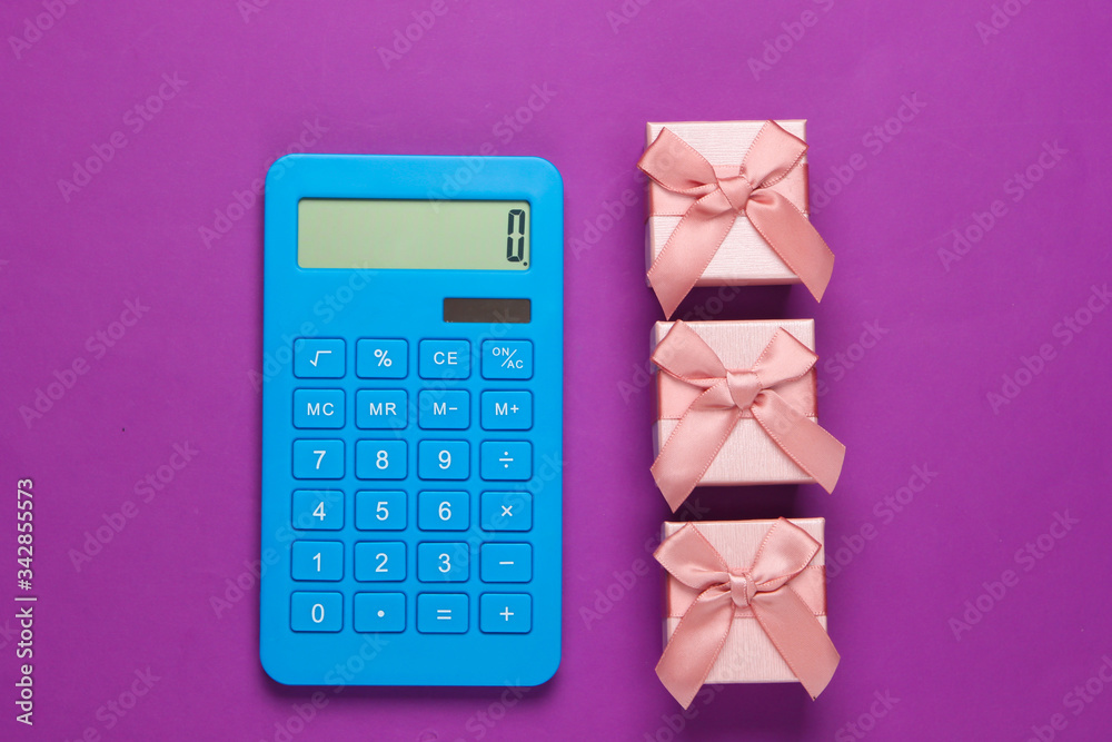 Calculator and gift boxes with a bow on purple background. Calculation of the value of the gift. Top view. Calculator and gift boxes with a bow on purple background. Calculation of the value of the gift. Top view.
