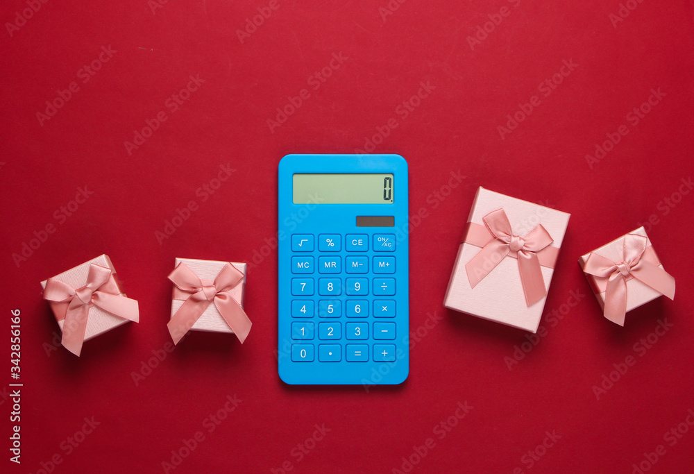 Calculator and gift boxes with bow on red background. Calculation of the value of the gift. Top view. Calculator and gift boxes with bow on red background. Calculation of the value of the gift. Top view.