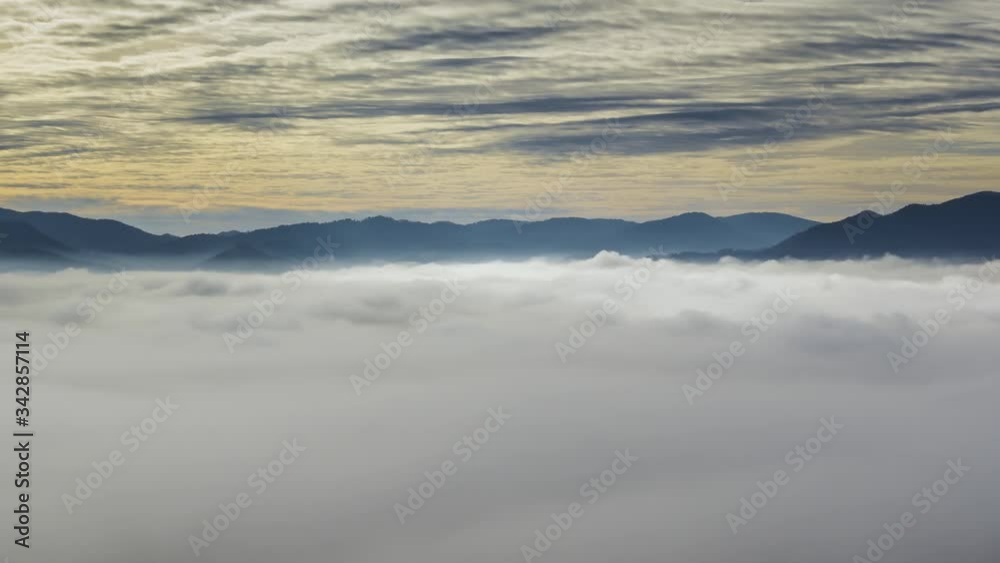Zoom out time lapse sunlight shining on low altitude fog. Colorful sunrise golden hour over cloud inversion. In distance mountain range Zoom out time lapse sunlight shining on low altitude fog. Colorful sunrise golden hour over cloud inversion. In distance mountain range