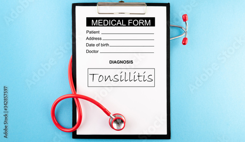 Tonsillitis - diagnosis in medical form. Stethoscope (red) and blank clipboard with a sheet of white paper on it on light blue backround. Medical concept. photo