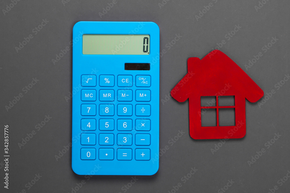 Calculation of the cost of rental housing. Red house figurine, calculator on gray background. Top view