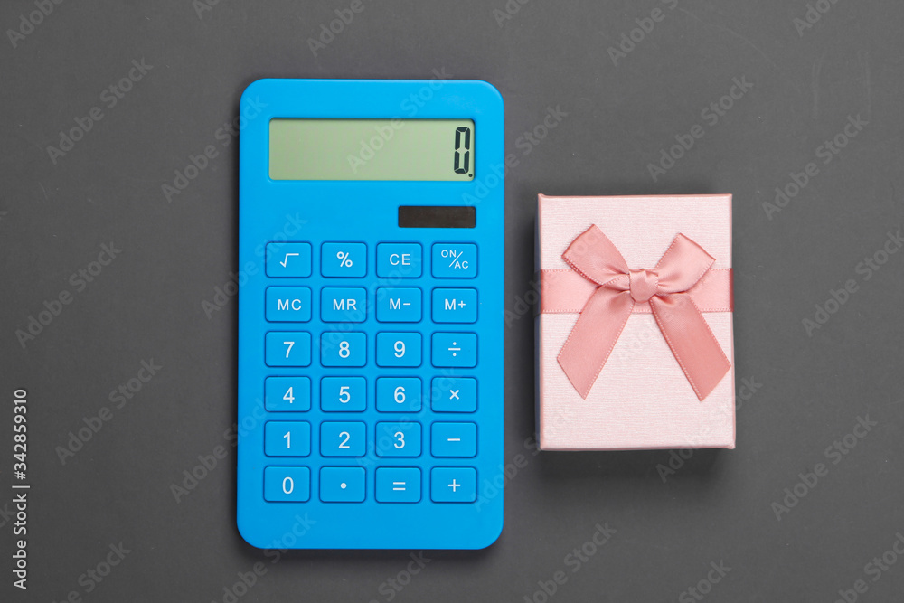 Calculator and gift box with bow on gray background. Calculation of the value of the gift. Top view. Calculator and gift box with bow on gray background. Calculation of the value of the gift. Top view.