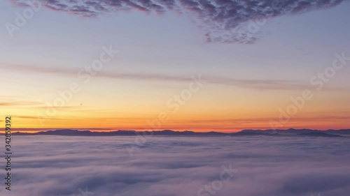 Zoom in time lapse over colorful inversion clouds. Amazing orange and yellow golden hour sunrise. Low altitude fog rolling over large basin. Vivid seascape sea of clouds