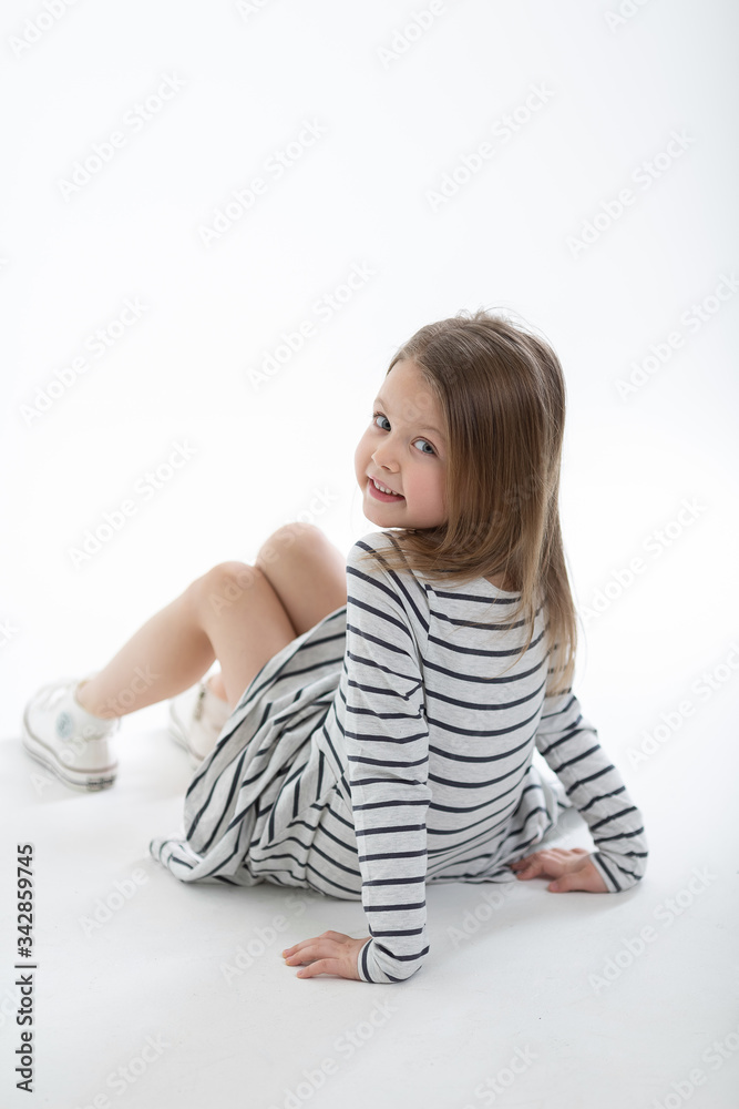 A cute little blonde with a mischievous cute smile is sitting on a white background.
