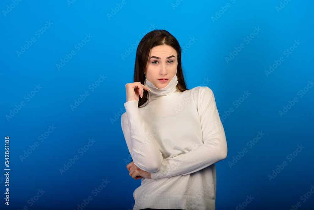 Portrait of a girl in a medical mask, which puts on a rubber glove. Blue background. Copy space. Portrait of a girl in a medical mask, which puts on a rubber glove. Blue background. Copy space.
