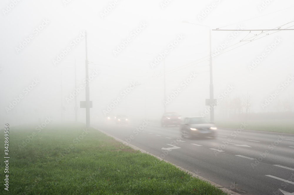 Cars riding on a city street in a foggy autumn morning