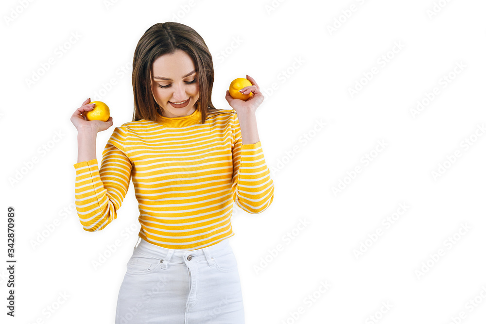 Sexy european brunette girl in a yellow sweater holds two lemons and stands isolated on a white background, beauty, skin care and detox concept Sexy european brunette girl in a yellow sweater holds two lemons and stands isolated on a white background, beauty, skin care and detox concept