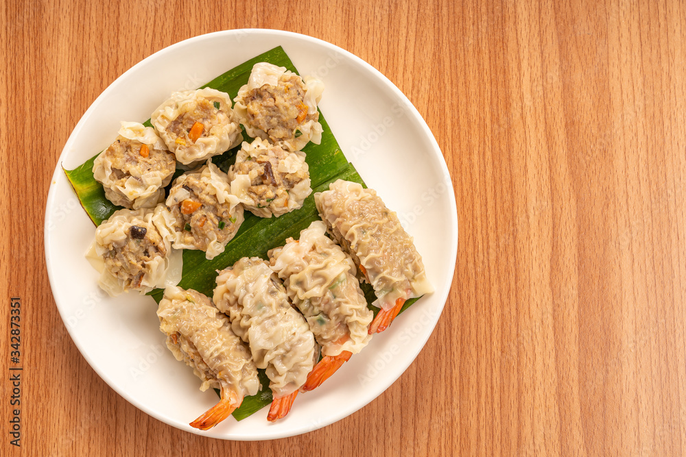 White Dish of Asian Steam Dumplings or Dim Sum a Famous Chinese Food with Pork and Shrimp on Wood Table. White Dish of Asian Steam Dumplings or Dim Sum a Famous Chinese Food with Pork and Shrimp on Wood Table.